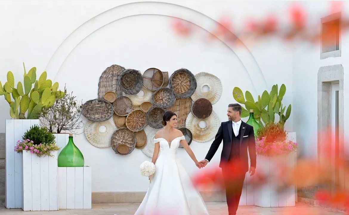 Destination Wedding in Portugal – Hochzeitspaar vor dekorativer Wand mit Körben, Pflanzen und mediterranem Flair