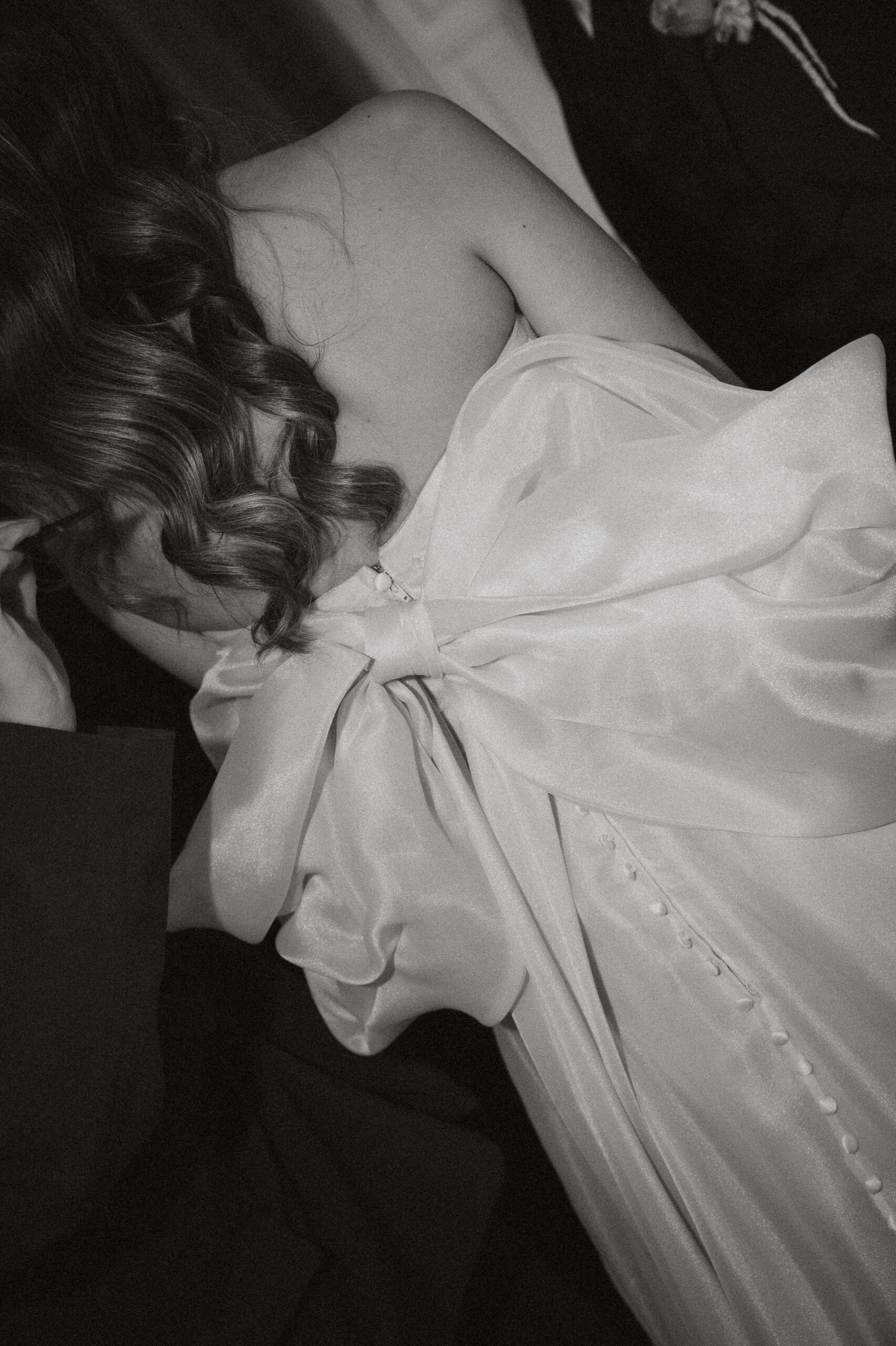 Braut von hinten mit eleganten Wellen und großer Schleife am Rückenausschnitt – Beleza Weddings & Events