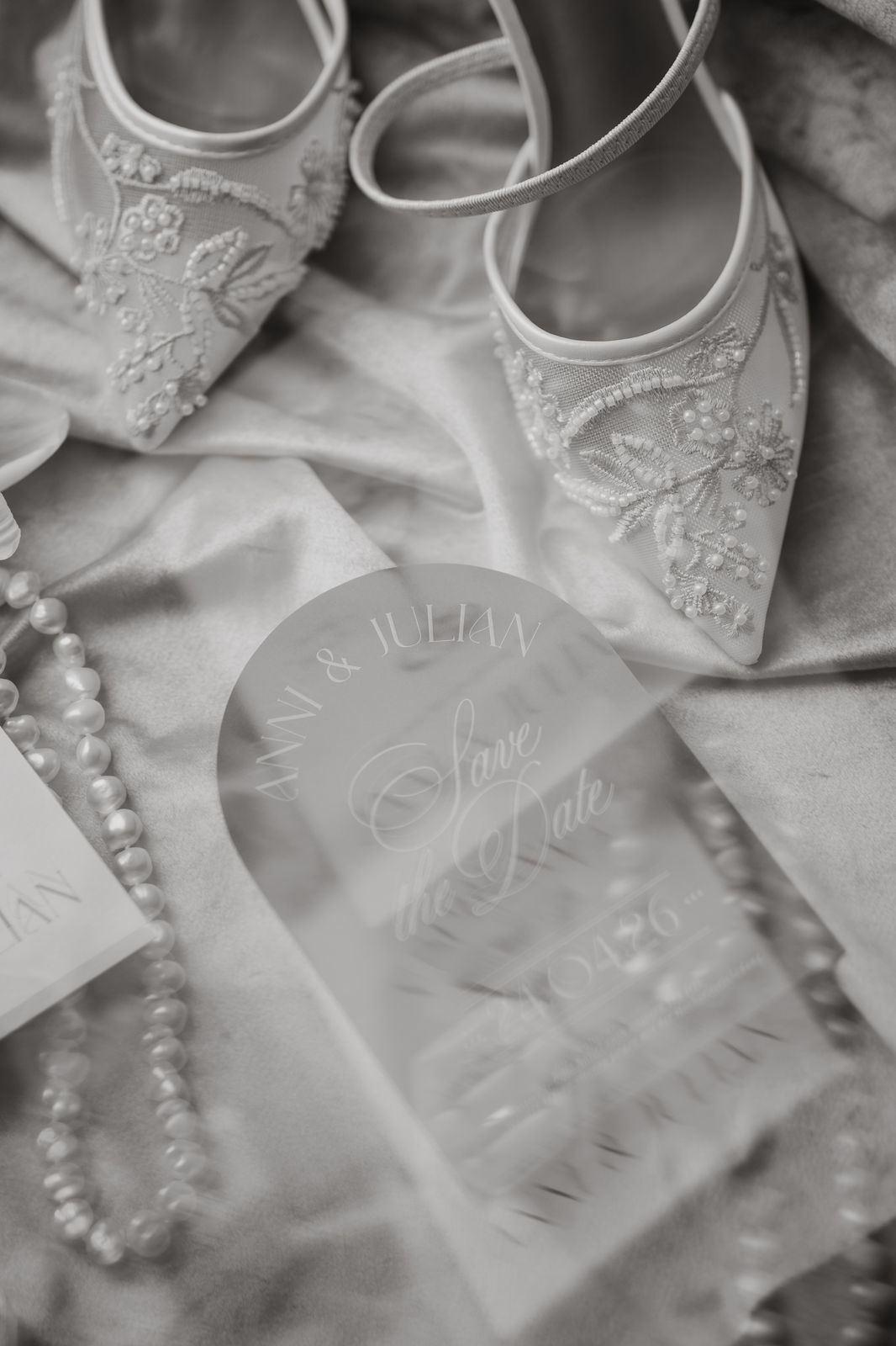 Eleganter Hochzeits-Flatlay mit bestickten Brautschuhen, Perlenkette und transparenter Save-the-Date-Karte – Beleza Weddings & Events